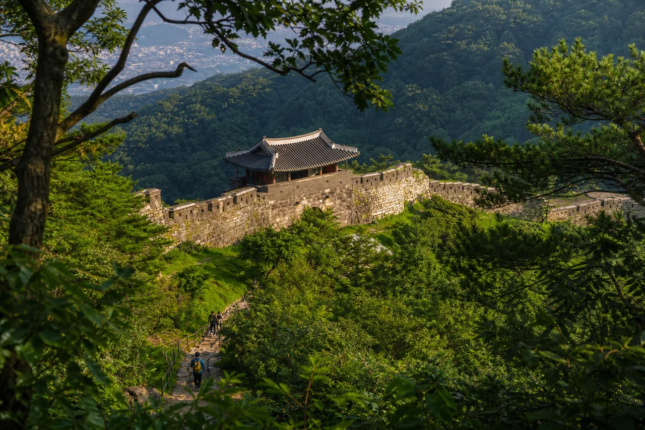 여름 숲 사이로 보이는 남한산성 성곽과 전통 문루, 산길 탐방객
